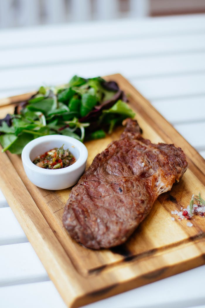 our-services-03 Juicy grilled steak served with fresh herb salad and sauce on a wooden board.