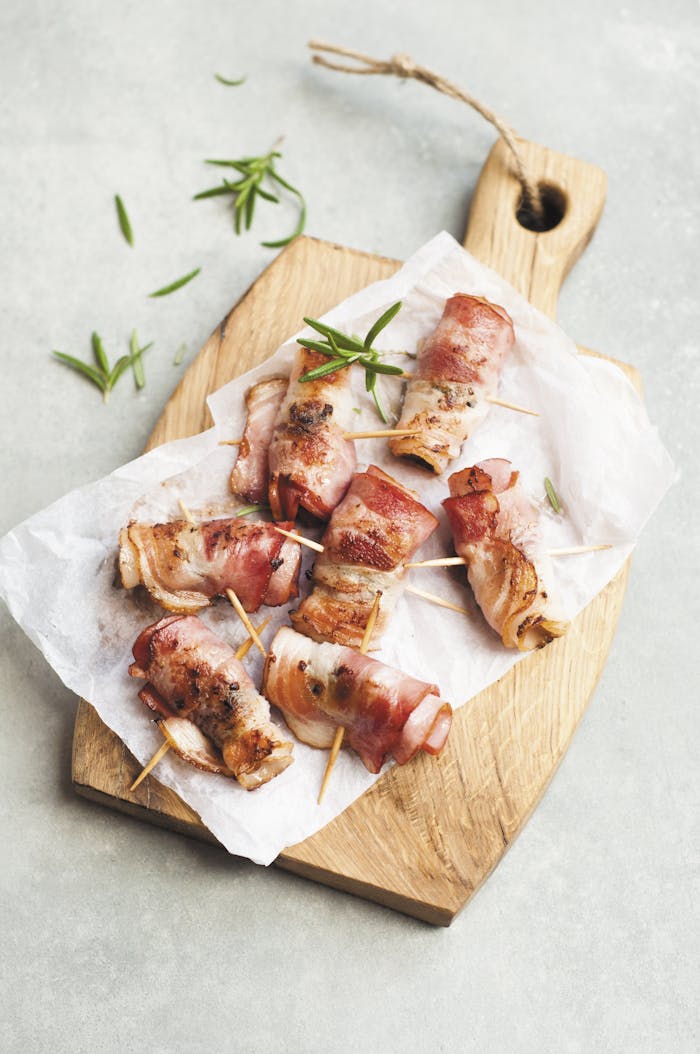 Delicious bacon wrapped chicken bites on a wooden board with herbs, perfect for a savory appetizer.