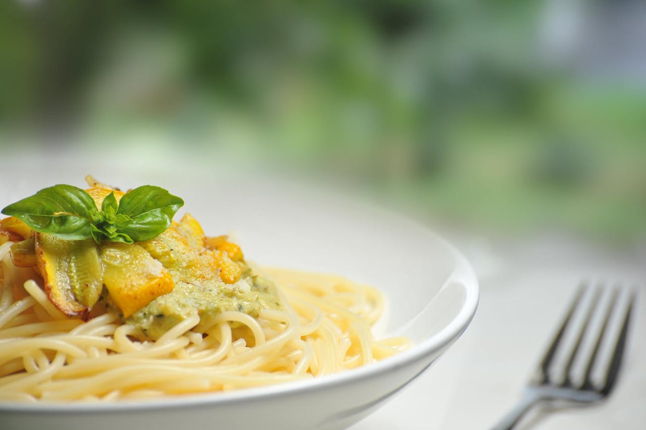 our-services-02 Close-up of freshly made spaghetti topped with basil and creamy pesto sauce in a white dish.